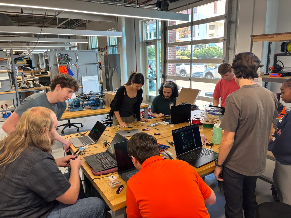 Students gathered around a long Makerspace bench covered in laptops, tools, and partly assembled radios.